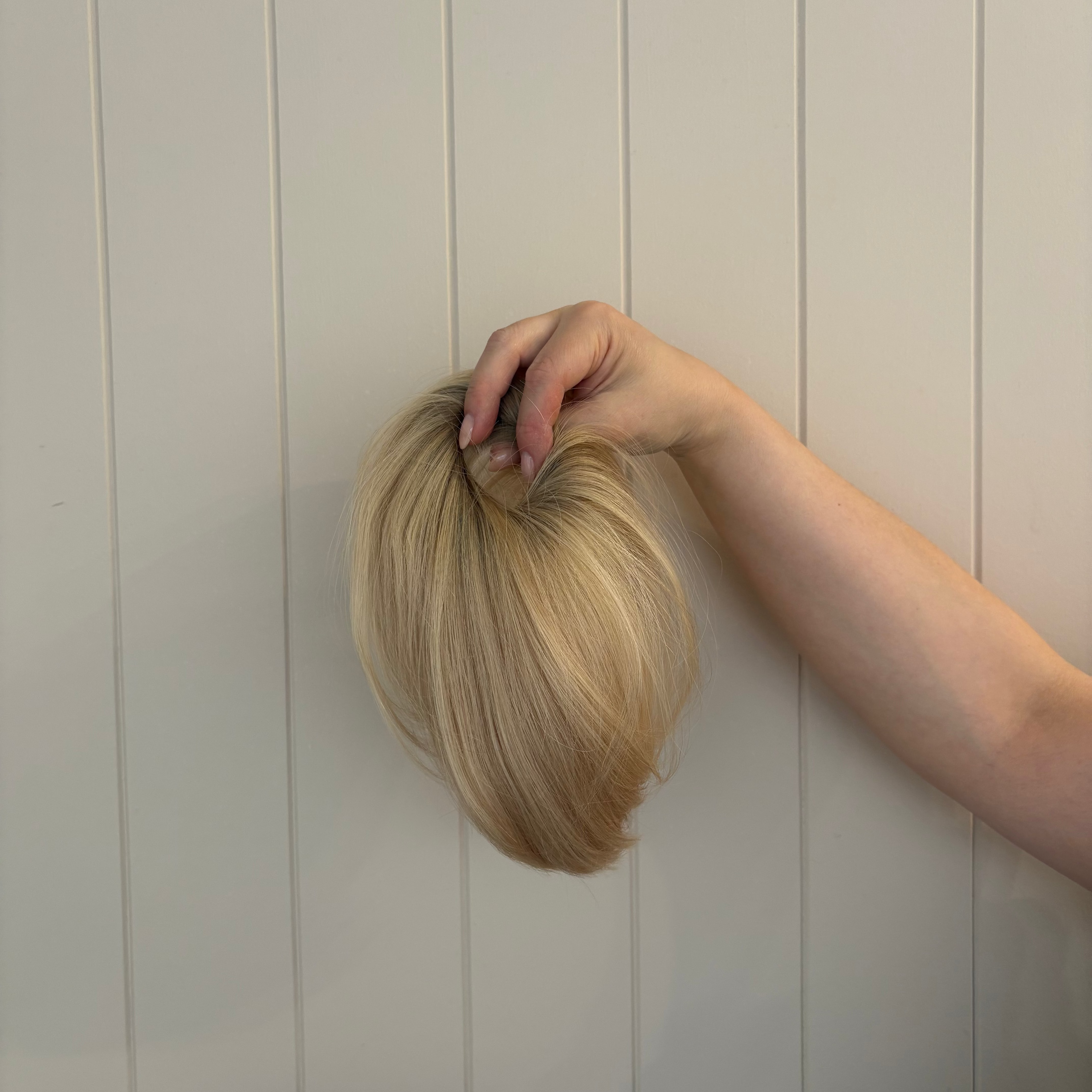Blonde hair held against a light wooden panel background